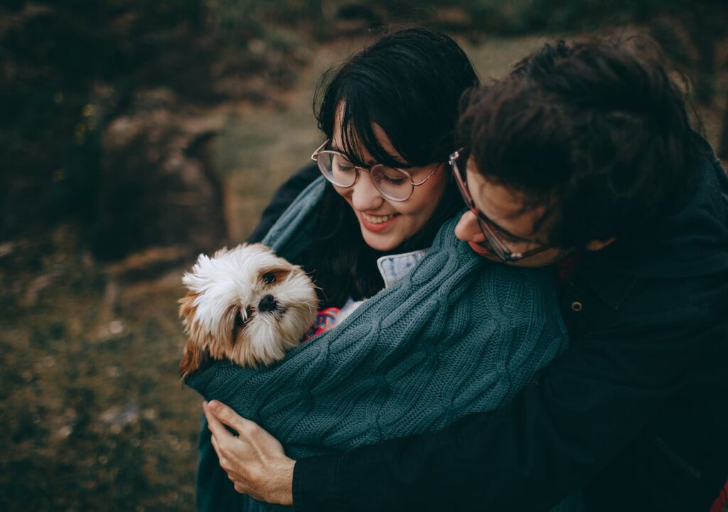 A happy couple cuddles their Shih Tzu dog outdoors, showcasing love and joy.
