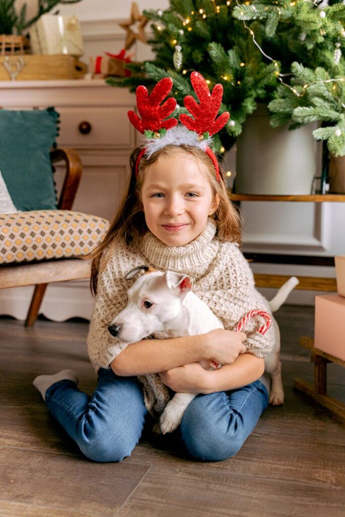 pexels photo 6057069 Smiling girl with reindeer headband hugging dog by Christmas tree indoors.